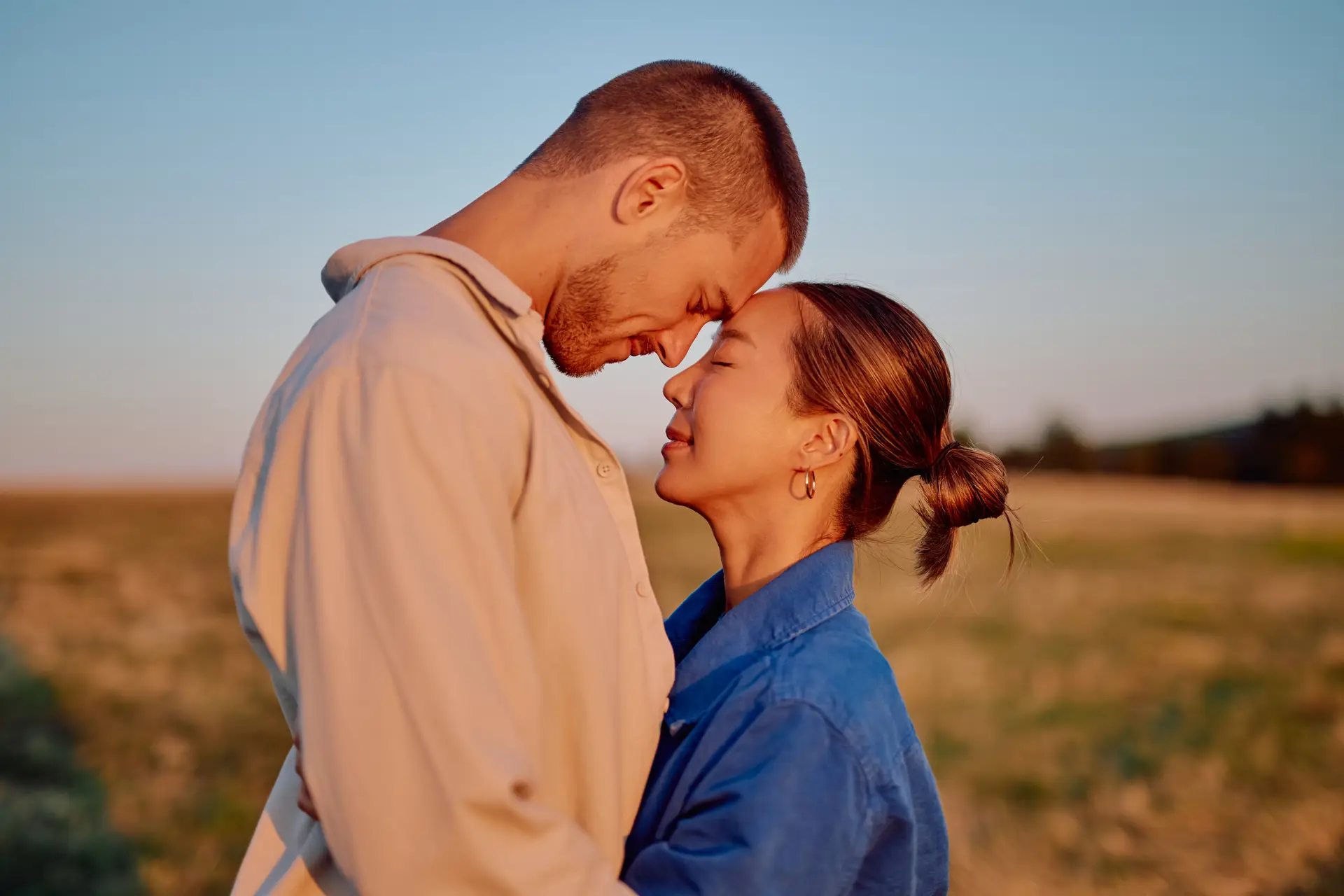 Romantic couple embracing in a field at sunset, enjoying intimacy and sharing a tender moment of love